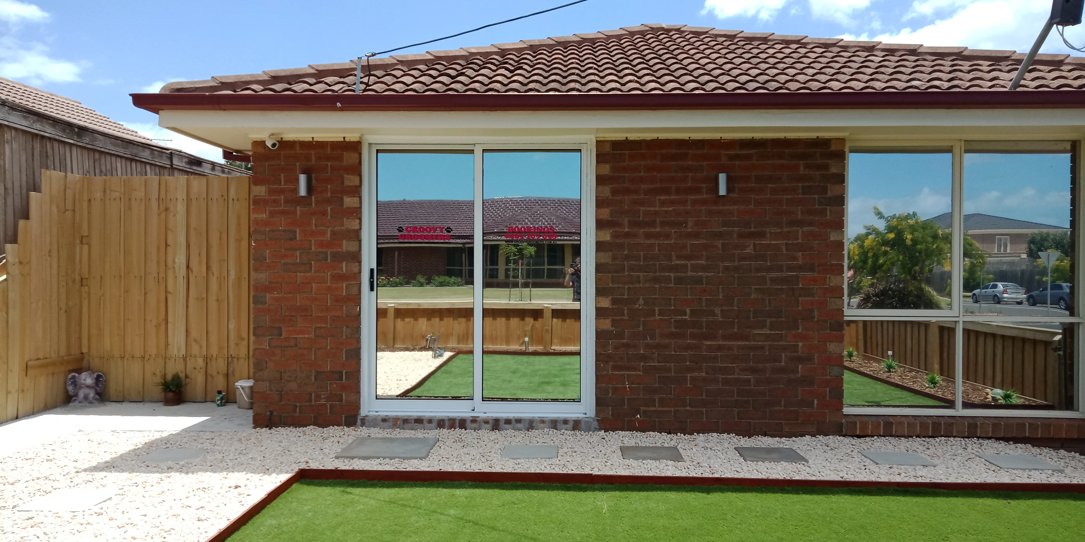 The exterior of the salon &mdash; sliding glass door, gravel and artificial-turf yard, koala ornament